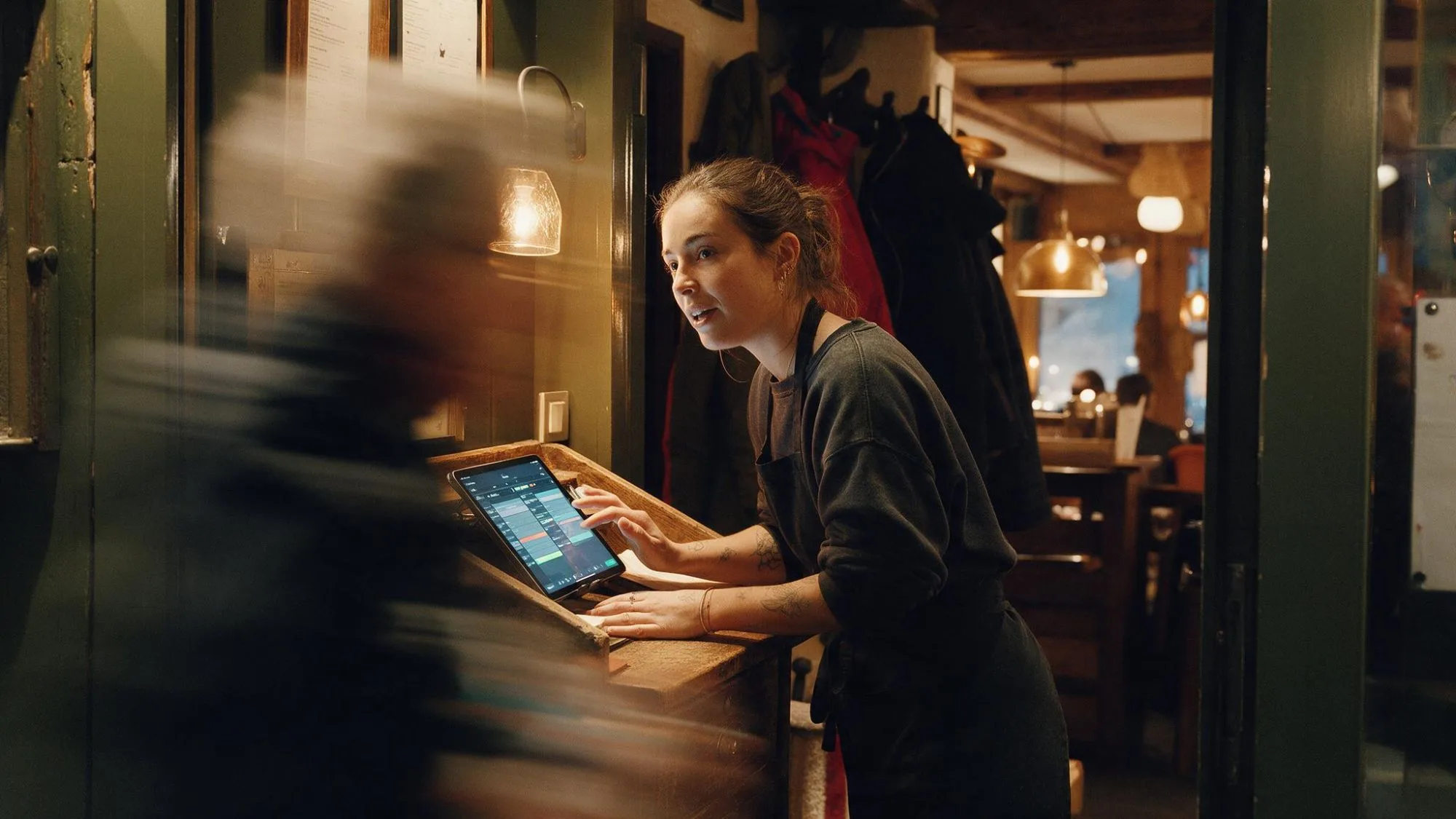 Een gastvrouw bij de deur van het restaurant bekijkt de reserveringen van vanavond op een tablet terwijl een gast binnenkomt